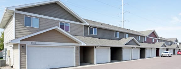 a row of townhomes with garages and cars parked in front of them