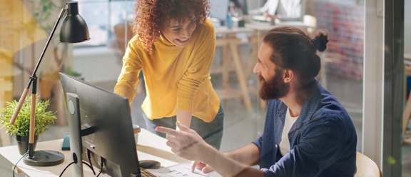 A man and a woman are working together at a desk in an office.
