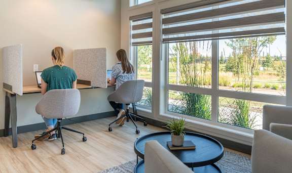 Two women are working at computers in a room with large windows.