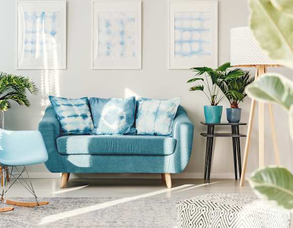 A living room with a blue couch, yellow pillows, and a red and white rug.