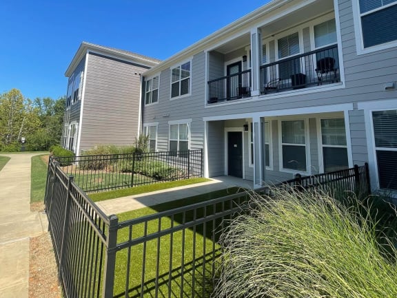 an apartment building with a grassy yard and a black fence at Watermark at Steele Crossing, Arkansas, 72703