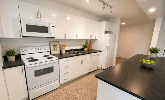 A modern kitchen with white cabinets and black countertops.