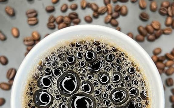 A cup of coffee with coffee beans scattered around it.