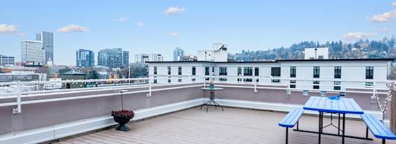 A wooden rooftop deck with a blue table and chairs overlooking a city skyline.