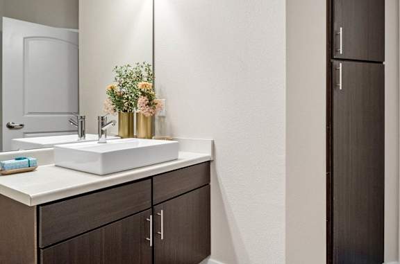 A bathroom with a sink, mirror, and brown cabinets.