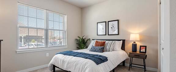 A bedroom with a bed, nightstand, and two framed pictures on the wall at Aventura at Wentzville I & II Apartments, Wentzville, MO