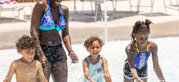 A woman and three children are playing in a pool.
