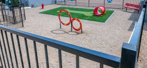 Fifteen 50 apartments Las Vegas Dog park with red park bench, fire hydrant, and dog play tubes and hoops. Features a large patch of artificial grass.