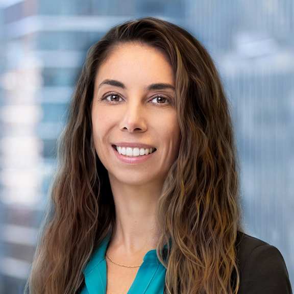 A woman with long brown hair wearing a teal blouse and black blazer.