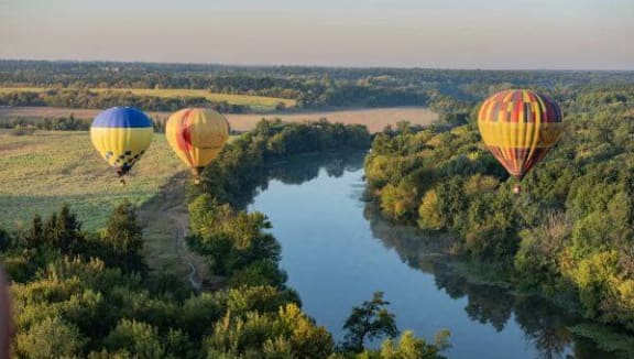 three hot air balloons flying over a river