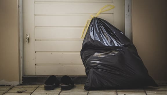 a black trash bag with a yellow ribbon next to a pair of shoes on a tiled