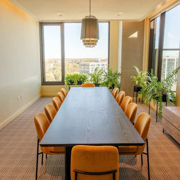 A long table with chairs and a hanging light fixture in a room with a view. at Scout Living, powered by Placemakr Apartments, Atlanta, GA, 30308