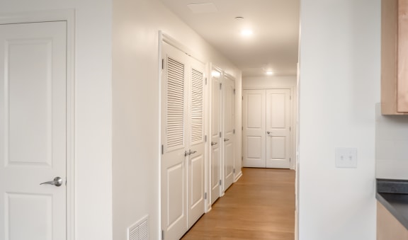 a long hallway with white closets and doors and a wood floor