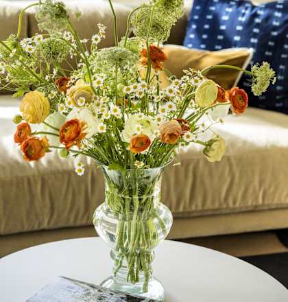 A vase of flowers sits on a table in front of a couch.