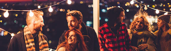 A group of people are standing together outside at night with string lights in the background.