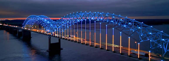 A bridge with blue lights is shown at dusk.