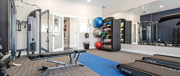 A well equipped gym with a mirrored wall and a variety of exercise equipment at Aventura at Wentzville I & II Apartments, Wentzville