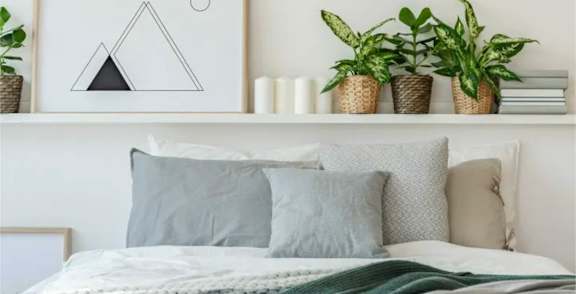 A bedroom with a bed, pillows, a framed picture, and potted plants.