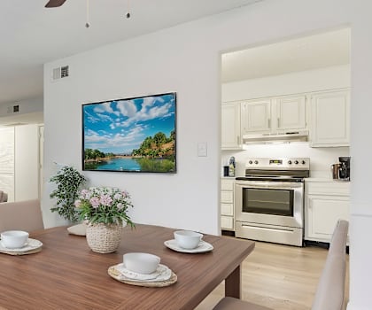 A living room with a wooden table and chairs, a television, and a painting on the wall.