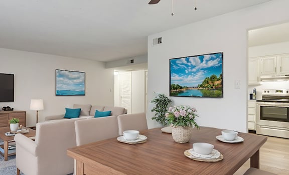 A living room with a wooden table and chairs, a television, and a painting on the wall.