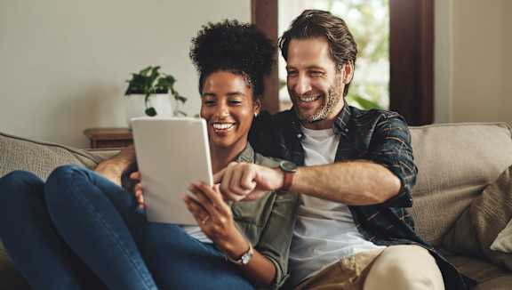 a man and woman sitting on a couch looking at a tablet computer