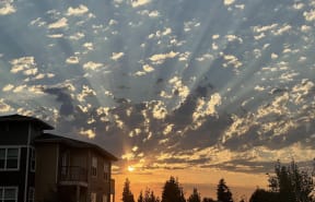 the sun sets over the horizon behind a house and clouds
