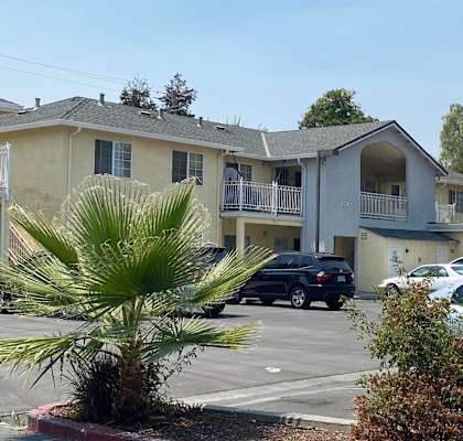 a large apartment complex with palm trees in the foreground and a parking lot in the background