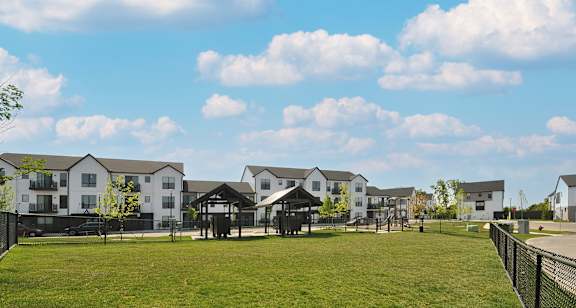 A grassy field with a fence and houses in the background.