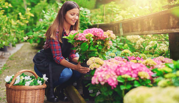 a woman crouching in a garden with a basket of flowers