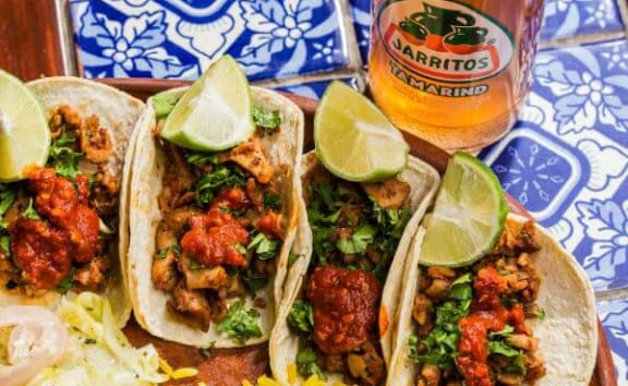 three tacos on a plate next to a glass of beer