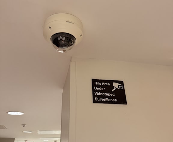 A security camera is installed on the ceiling above a sign that reads