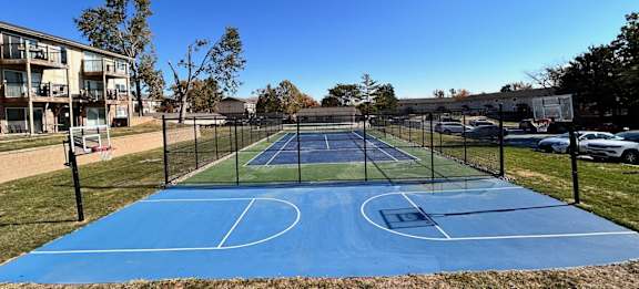 A blue tennis court surrounded by a fence, located within the Cambridge Apartments community.