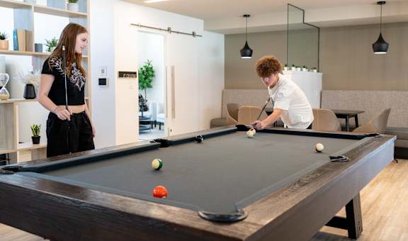 A man and a woman are playing pool in a room with a pool table.