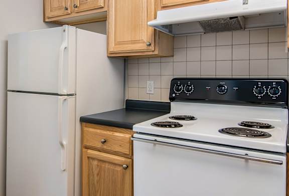 A kitchen with a white refrigerator, white stove, and wooden cabinets.