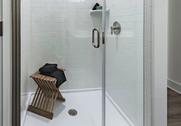 a walk in shower with white tile and a glass door with a towel rack on the side