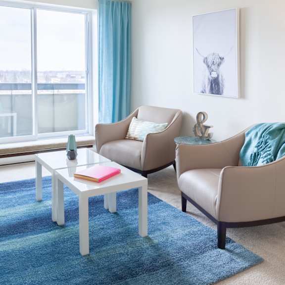 A living room with a blue rug and a white coffee table.
