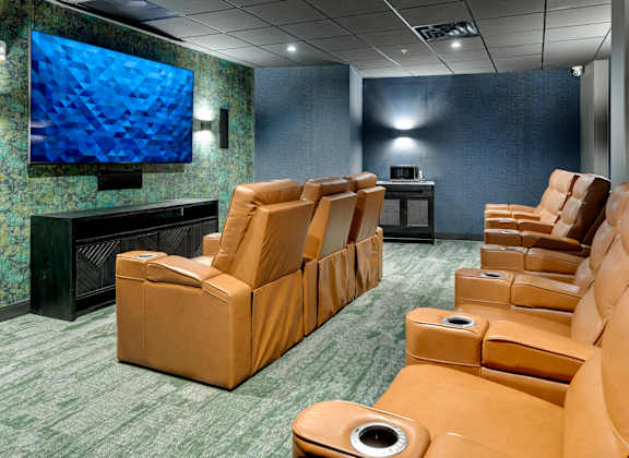A row of brown recliner chairs are lined up in a room with a large screen television.