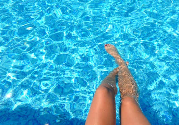 A person's legs are submerged in clear blue water.
