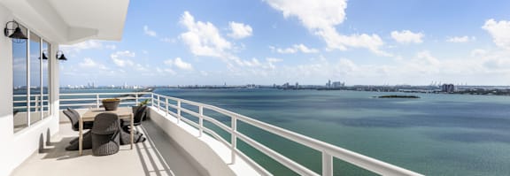 A white balcony with a table and chairs overlooking a body of water. at The Hamilton, Miami, Florida