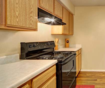 A cozy kitchen with black appliances, a red rug, light countertops with lots of room, and light wooden cabinets with decorations at Summit Point Apartment Homes. 