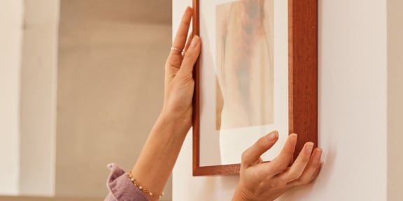 a person hanging a picture frame on a wall