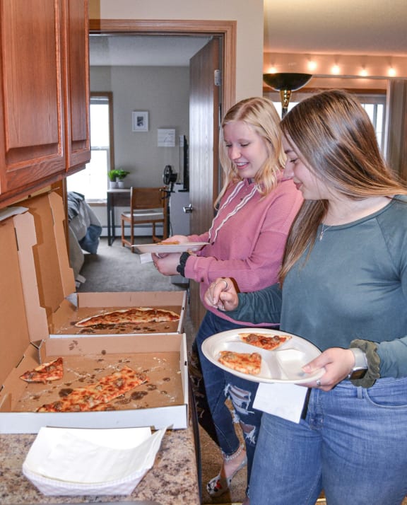 two women standing in a kitchen eating pizza at Summit Ridge, Duluth, MN