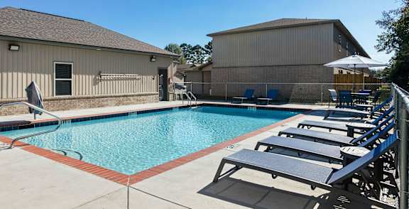 A pool with sun loungers and a building in the background.