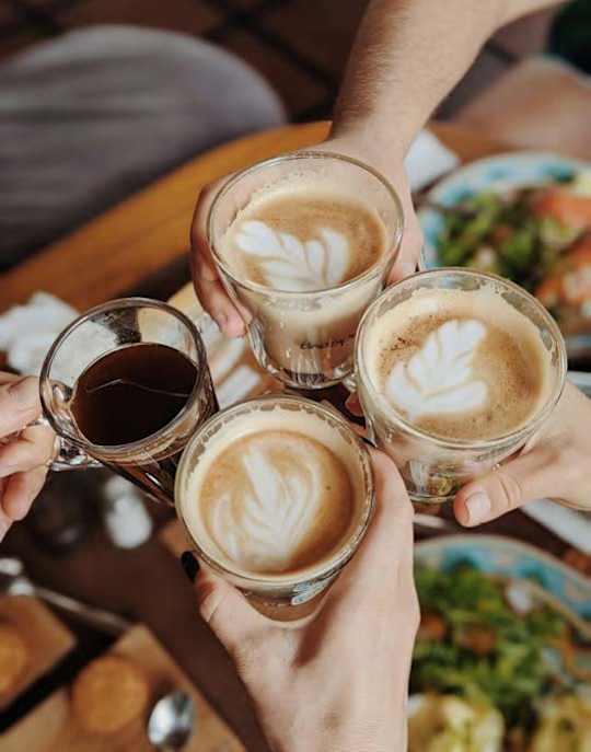 Four people toasting with coffee in clear glasses.