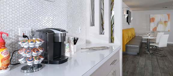 Fifteen 50 apartments Las Vegas clubhouse coffee corner with Keurig and coffee cups on counter with modern white penny tile backsplash.