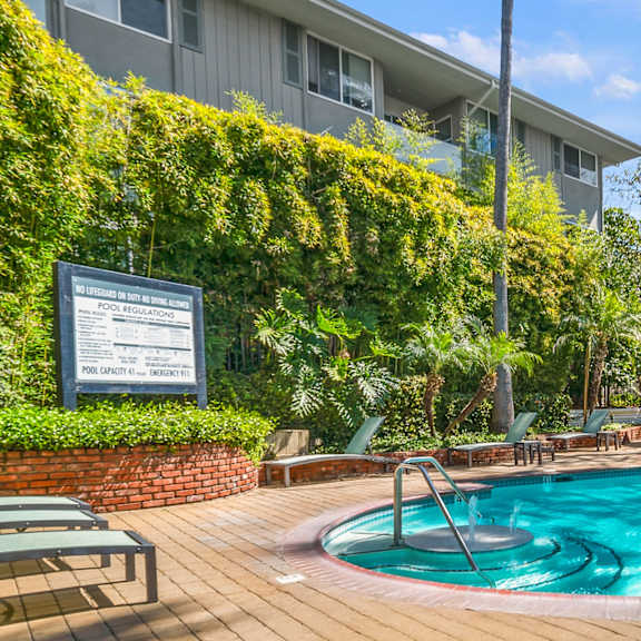 A pool surrounded by a wooden deck and green trees.