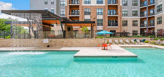 A large swimming pool in front of a multi-story apartment building.