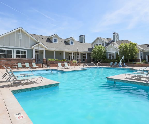 Big spacious pool with lawn chairs and club house in the background.