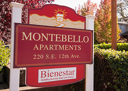 A sign for Montebello Apartments stands in front of a bush.