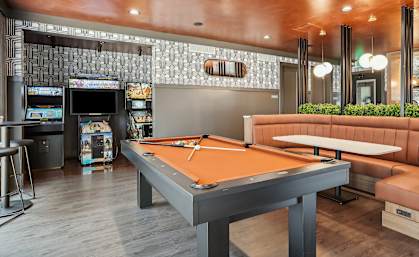 A pool table is in the middle of a room with a bar and a row of TVs on the wall.